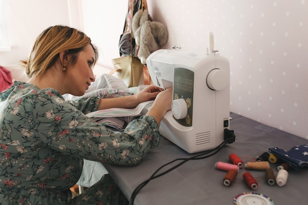 Una niña cose en una máquina de coser en casa. La vista posterior es un pasatiempo favorito. Producción propia de ropa.