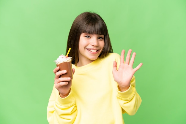 Niña con crema de chocolate sobre fondo de clave de croma aislado saludando con la mano con expresión feliz