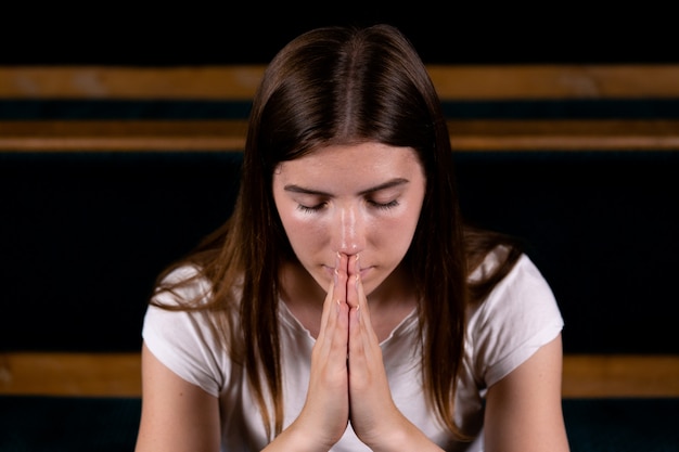 Una niña cristiana con camisa blanca está sentada y rezando con humilde corazón en la iglesia