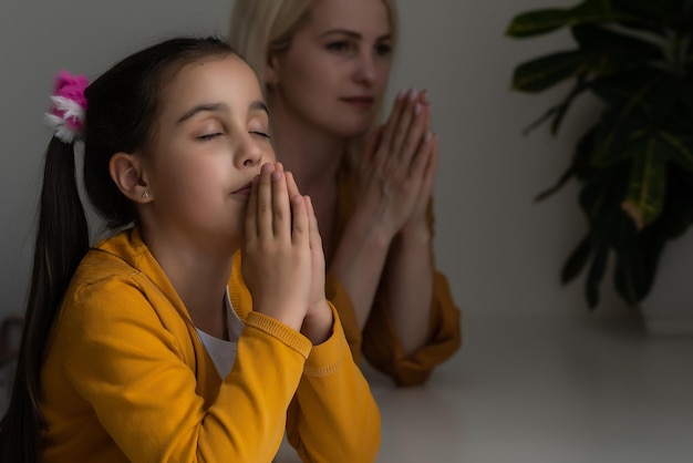 Niña cristiana religiosa y su madre orando en casa.