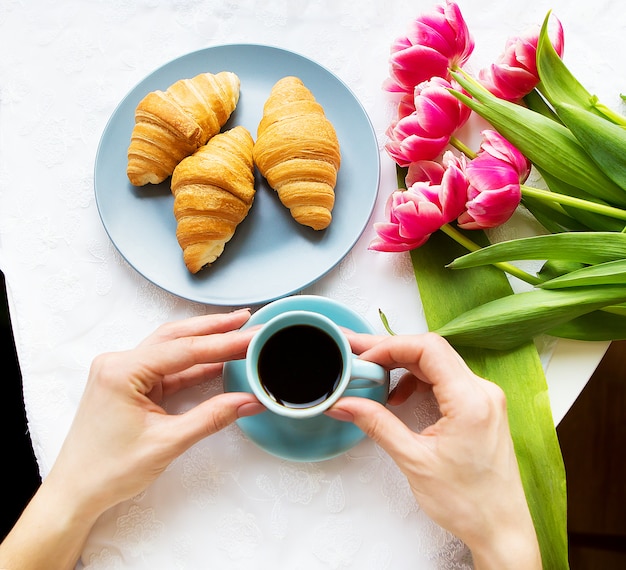 Niña con croissants y café, un ramo de tulipanes rosados, feliz mañana