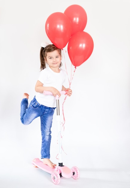 Una niña de cuatro años viste un estilo deportivo y sostiene un scooter para niños fotografiado sobre un fondo blanco.