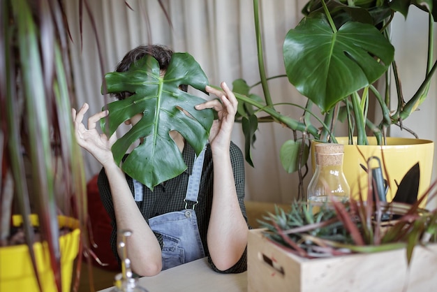 Una niña se cubre la cara con hojas verdes para divertirse y relajarse plantas caseras en el balcón gen z