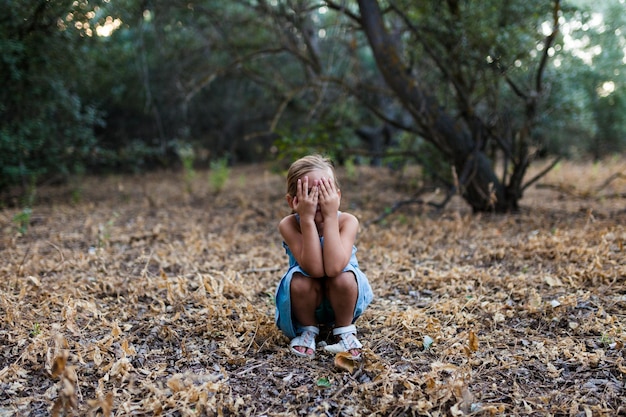 Niña cubriendo la cara mientras se agacha en el bosque