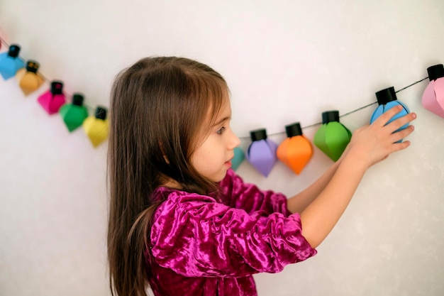 Niña cuelga una guirnalda de papel hecha a mano en la pared