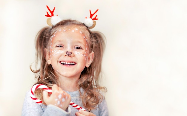 una niña con cuernos de Navidad sosteniendo una piruleta y riendo