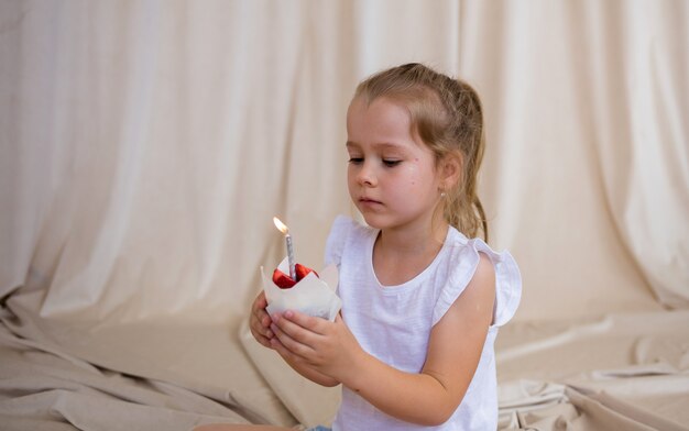 Niña cumpleañera sostiene un cupcake con una vela sobre un fondo beige con una copia del espacio