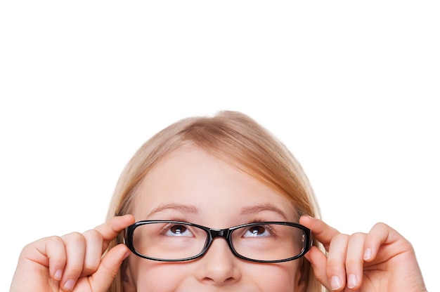 Niña curiosa. Imagen recortada de una niña alegre ajustando sus gafas y mirando hacia arriba mientras está aislado en blanco