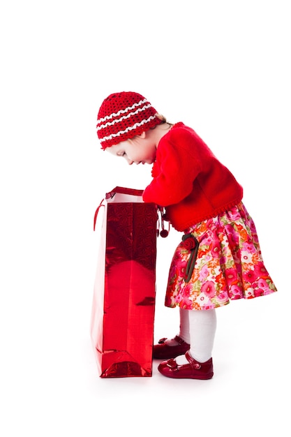 La niña curiosa del vestido rojo se ve en la bolsa roja aislada en blanco