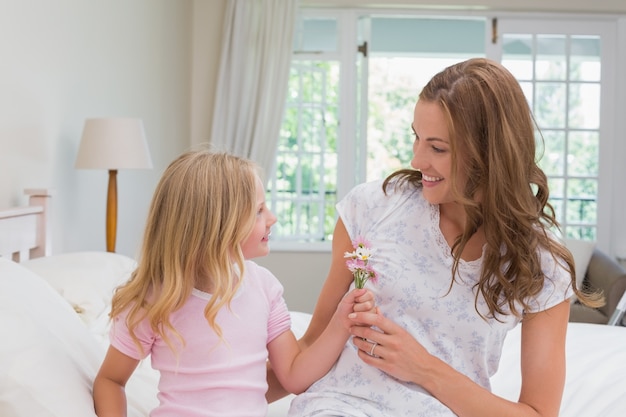 Niña dando flores a su madre en el dormitorio