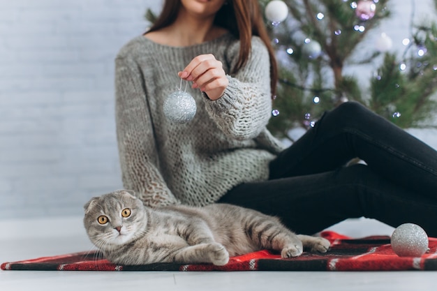 Una niña decora un árbol de Navidad y juega con su gato.