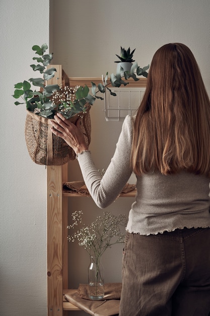 La niña decora un estante de madera con una bolsa ecológica con ramas de eucalipto, flores, plantas de interior.