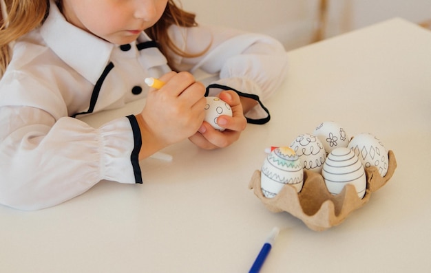 Una niña decora un huevo de PascuaEl niño dibuja con un rotulador sobre un huevo centrado en la tarea