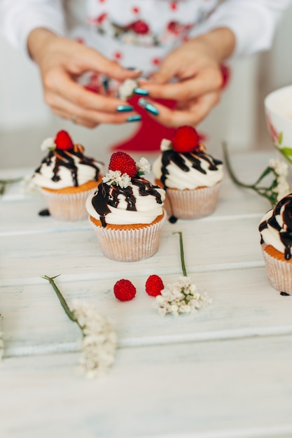 Una niña decora pastelitos con bayas frescas y flores.