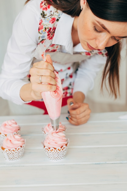 Foto una niña decora pastelitos con crema.