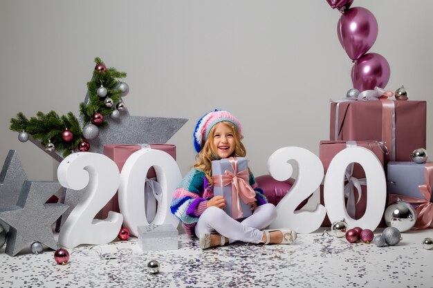 niña en decoración navideña en luz, cajas de regalo, números grandes 2020, año nuevo y Navidad