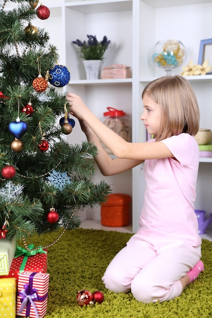 Niña decorando el árbol de Navidad en la habitación