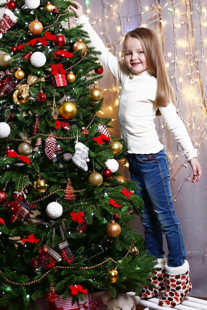 Niña decorando el árbol de Navidad sobre fondo brillante