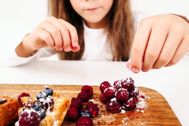 Niña decorando pasteles con frutos rojos