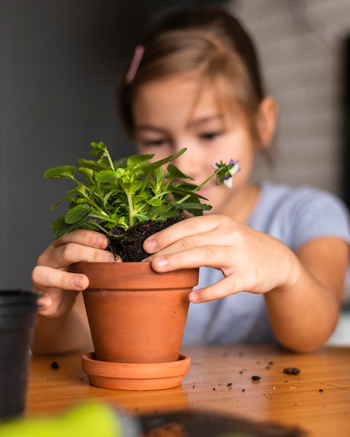 Foto niña defocused plantando flores en maceta en casa