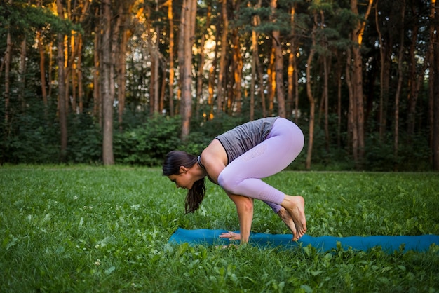 Una niña deportista realiza una pose Bakasana del yoga en la naturaleza