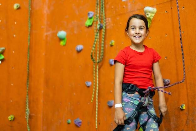 Niña deportiva escalada de rocas artificiales en la pared práctica en el gimnasio