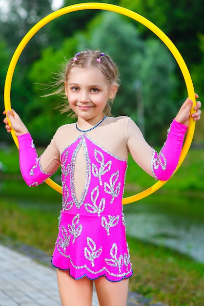 Niña deportiva haciendo ejercicio con hula hoop sobre fondo de parque