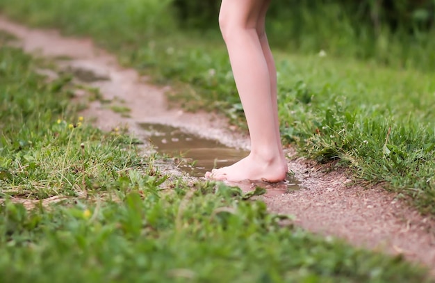 Niña descalza camina a través de charcos de agua después de la lluvia de verano en el campo.