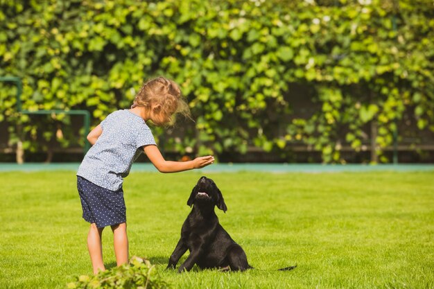 Niña descalza juega con un adorable cachorro labrador negro