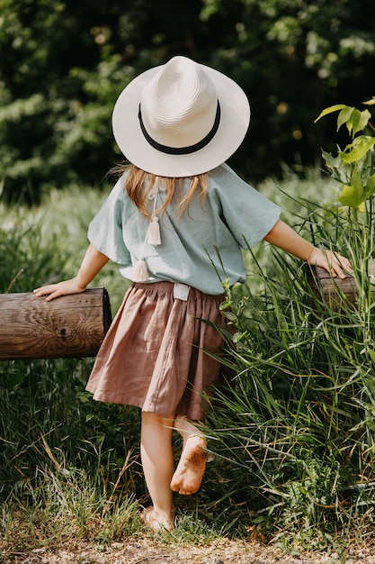 Niña descalza con un sombrero de paja, de pie en una hierba alta en un campo