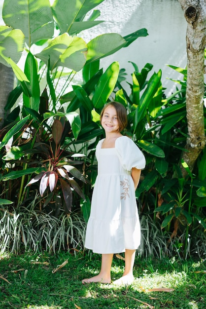 Niña descalza en un vestido blanco de pie en un jardín tropical