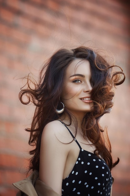 Niña descansando en el pueblo cerca de las caballerizas, retrato de una mujer al sol, estilo rústico. Retrato de una morena sexy con un impermeable en la naturaleza. Maquillaje perfecto, cosmética natural