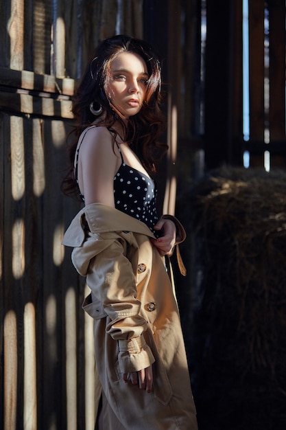 Niña descansando en el pueblo cerca del heno, retrato de una mujer al sol, estilo rústico. Retrato de una morena sexy en el pajar. Maquillaje perfecto, cosmética natural