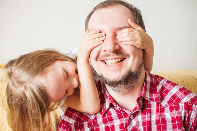 La niña desea a papá feliz el día de padre. Hija abraza a papá, cierra los ojos con las manos.