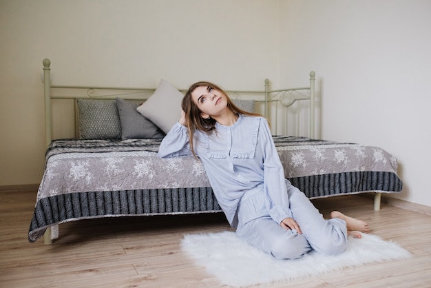 La niña se despertó y se sentó en pijama en la cama de su habitación. Elegante interior de color blanco grisáceo.