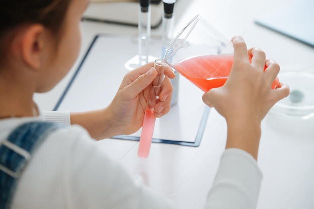 Niña de detrás haciendo proyecto de ciencia, vertiendo líquido rojo en un matraz