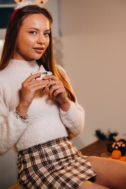 Una niña en el día de Navidad está sentada en la mesa de la cocina y sosteniendo una copa de champán.Mujer en la víspera de año nuevo con champán