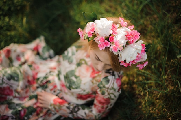 Niña en una diadema de flores sentado en el césped