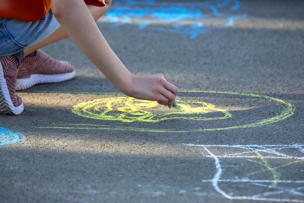 La niña dibuja una carita sonriente con tiza amarilla en el pavimento Creatividad y pasatiempos de entretenimiento y recreación infantil