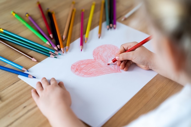 Foto niña dibuja un corazón rojo