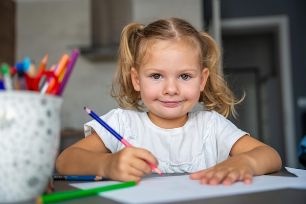 La niña dibuja con lápices de colores en casa.