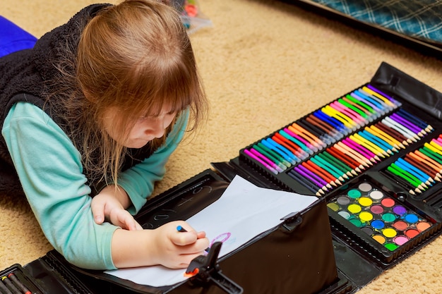 Niña dibuja con lápices de colores mientras está acostada en el piso niña dibuja lápices