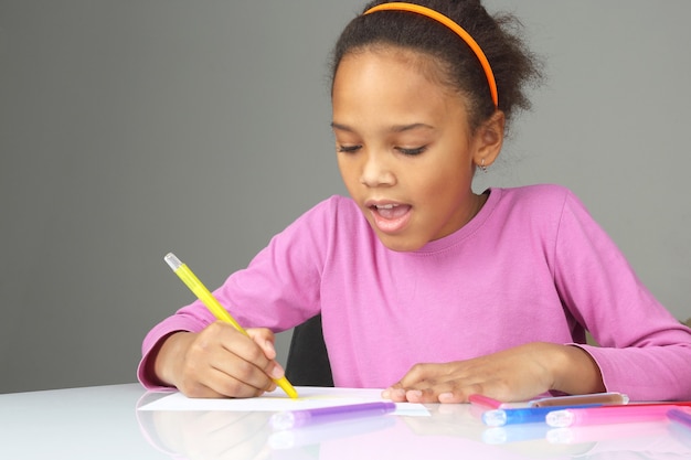 La niña dibuja un lápiz amarillo sobre papel blanco.