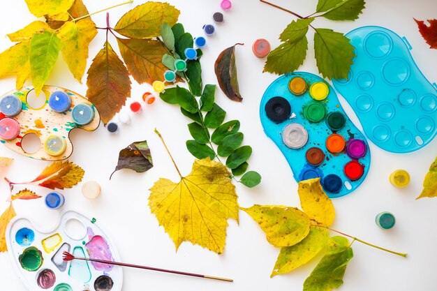 niña dibujando con pintura sobre hojas de otoño en la mesa.