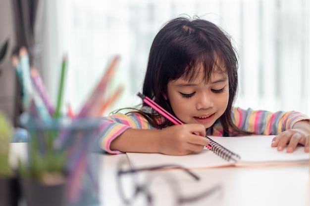 Niña dibujando en su libro y divirtiéndose en la mesa de juego Niño aprendiendo a colorear en casa o en el jardín de infantes