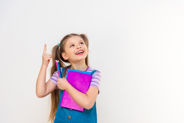 Una niña con diferentes libros en sus manos señala con el dedo el anuncio.