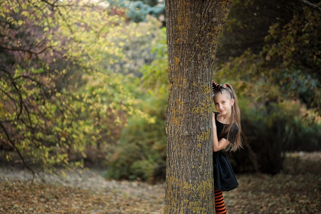 una niña en un disfraz de bruja para Halloween una niña mira desde detrás de un árbol