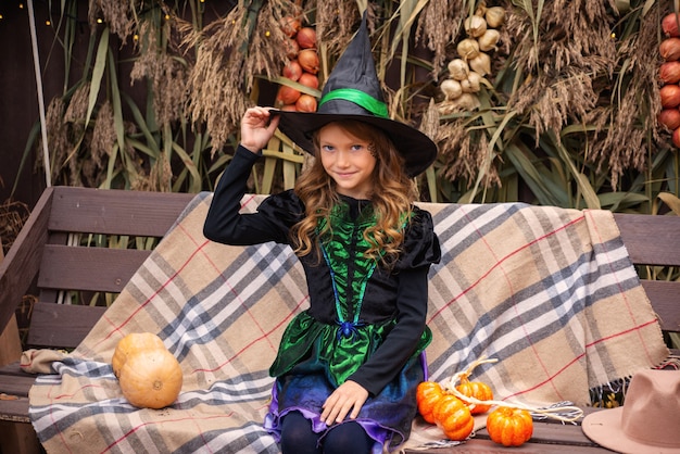 una niña con un disfraz de bruja lanza una magia sobre una calabaza en halloween