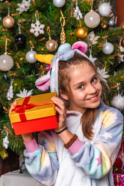 Una niña con un disfraz casero se sienta cerca del árbol de Navidad y tiene regalos