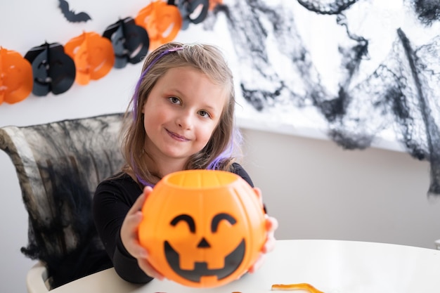 niña disfrazada de bruja sosteniendo un gato de calabaza con dulces, Halloween